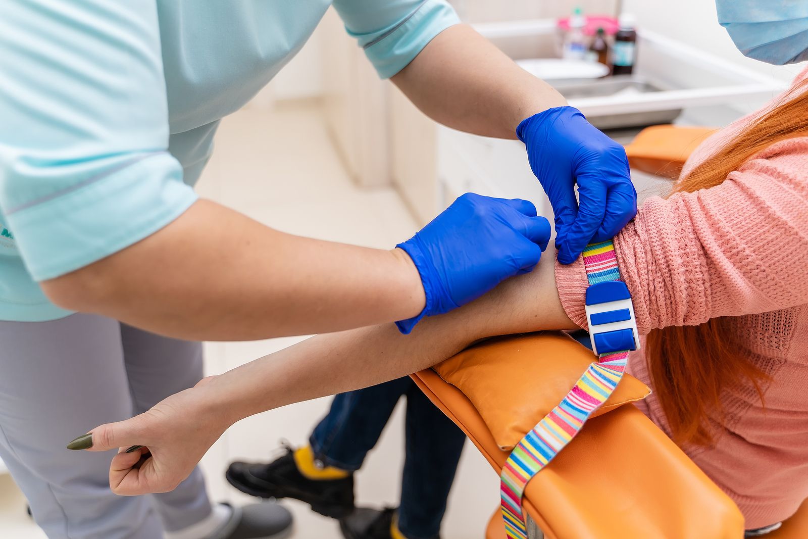 A nurse applying a tourniquet to a patient's arm to prepare for a preventive blood draw