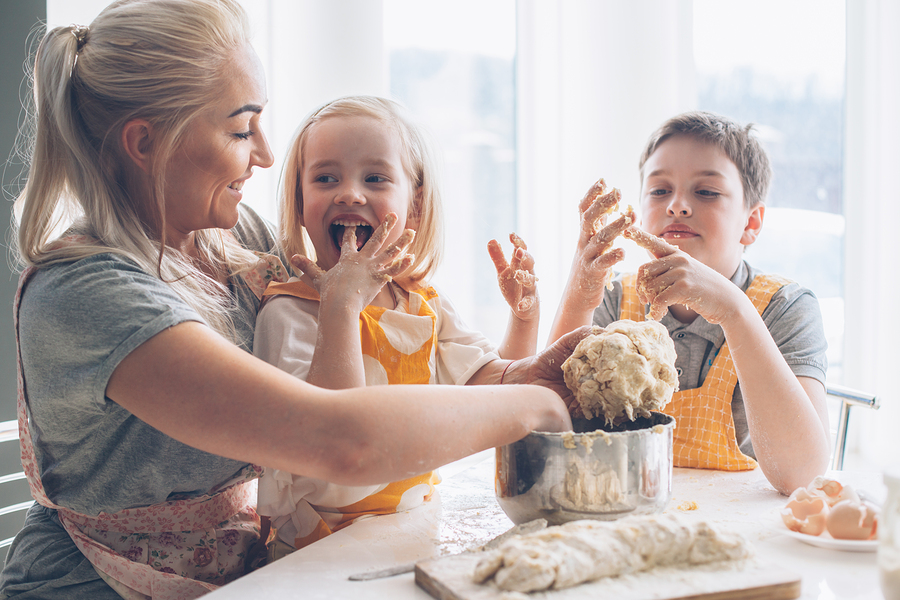A mother and her two children laughing while baking together in a bright kitchen