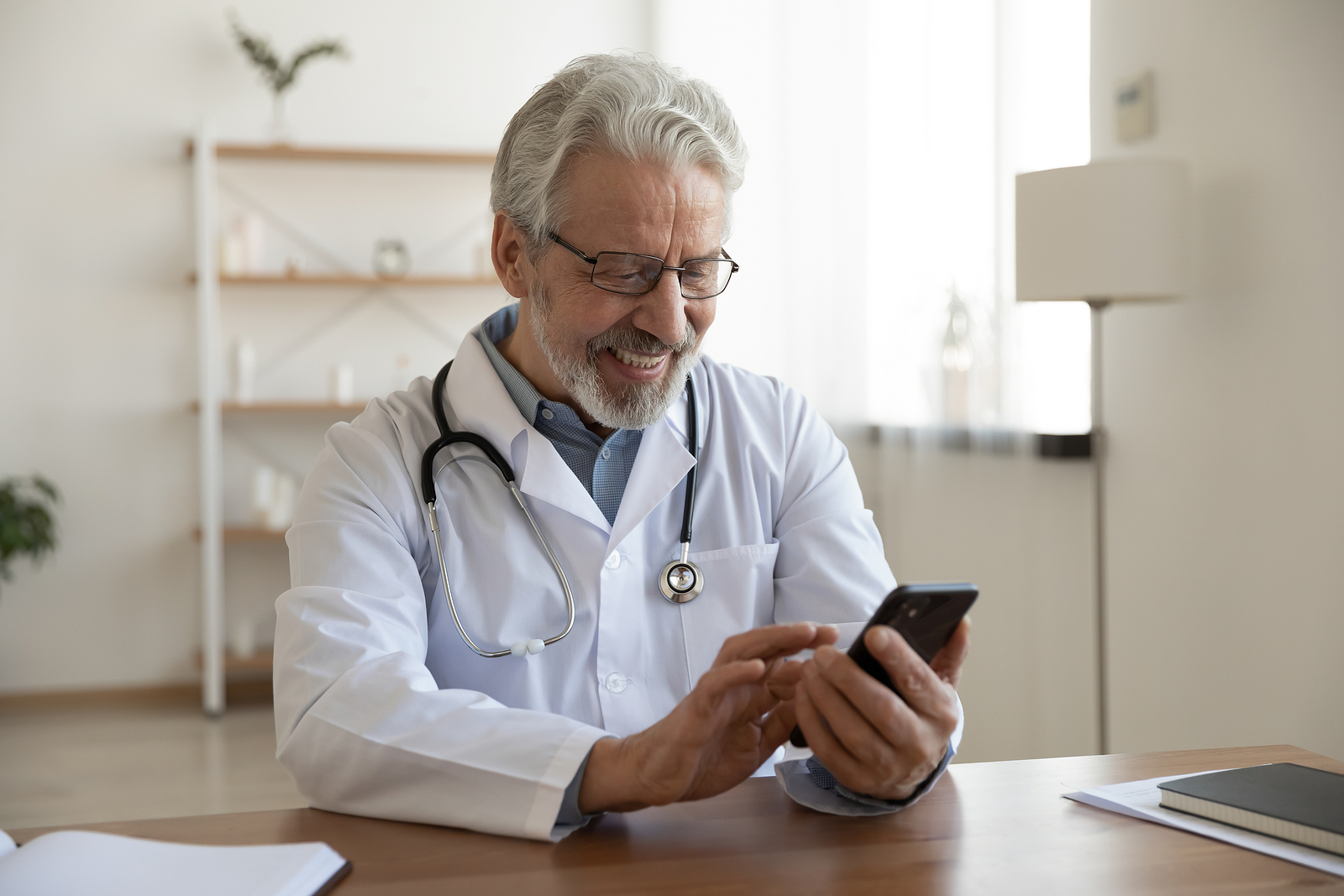 Smiling Lyric primary care physician using a smartphone to connect with a member