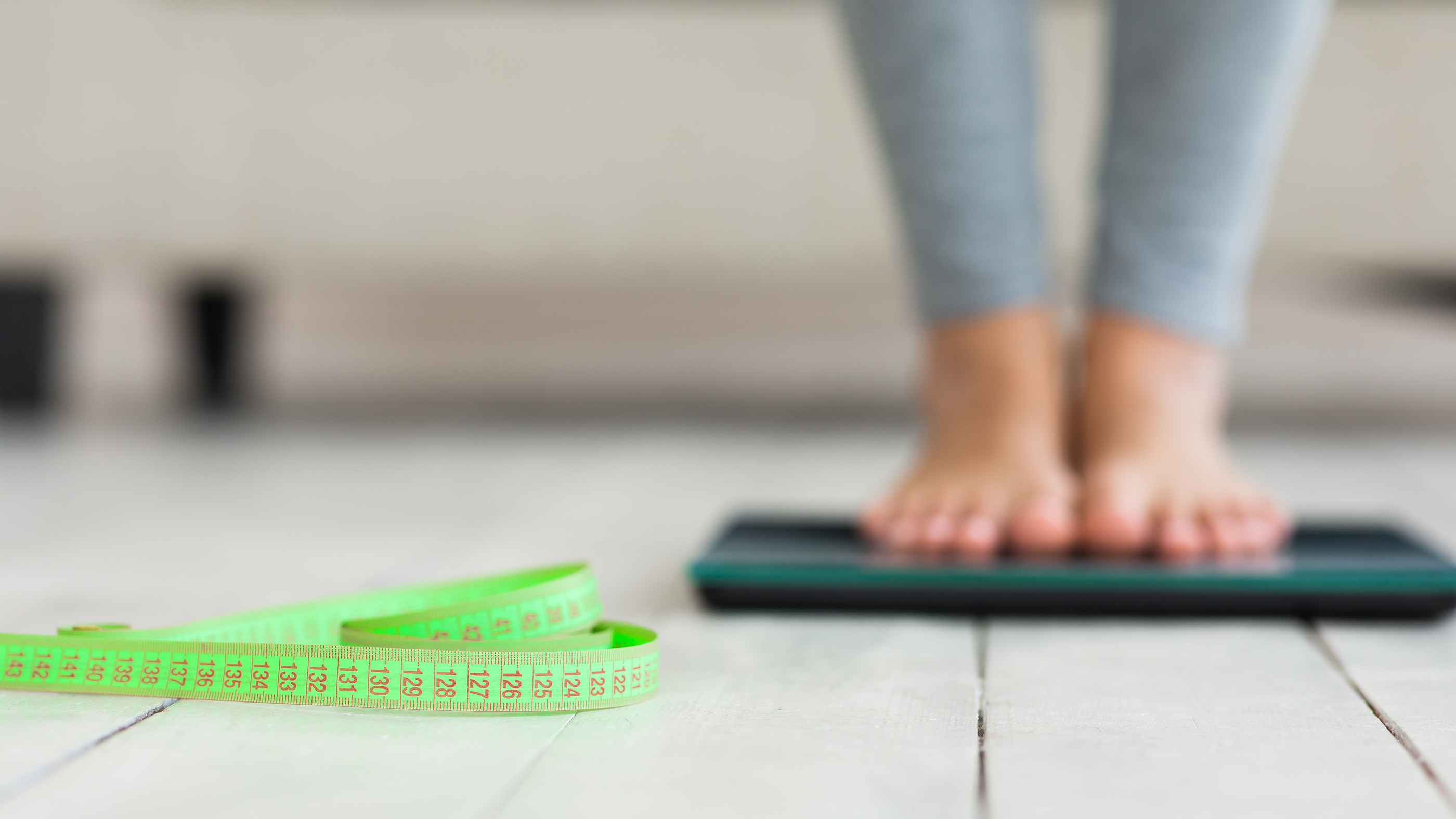 A person standing barefoot on a digital scale with a measuring tape on the floor